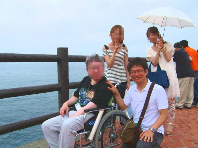 写真5：波が打ち寄せる海岸を、お客様はヘルパーと一緒に車椅子でゆっくりと進んでいます。岸壁に手が届きそうです。