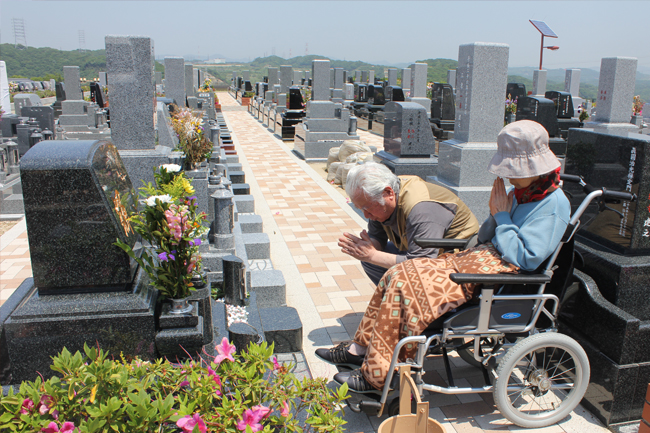 写真：お墓に手を合わせる二人。車椅子をお使いの奥さま。