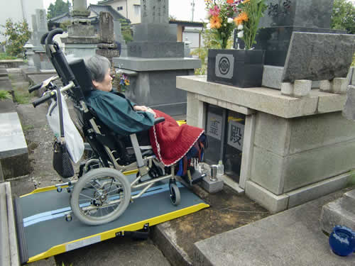 写真：車椅子に乗り、お墓の前で手を合わすお客様